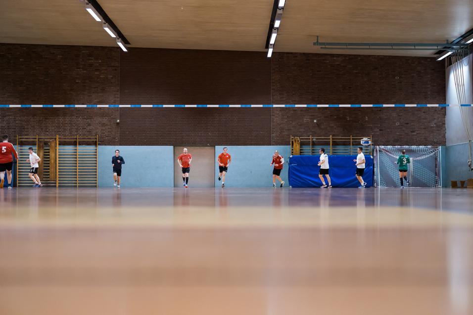 Fünf Spieler in Sportkleidung trainieren in einer Sporthalle, mit einem Tor und blauen Wänden im Hintergrund.