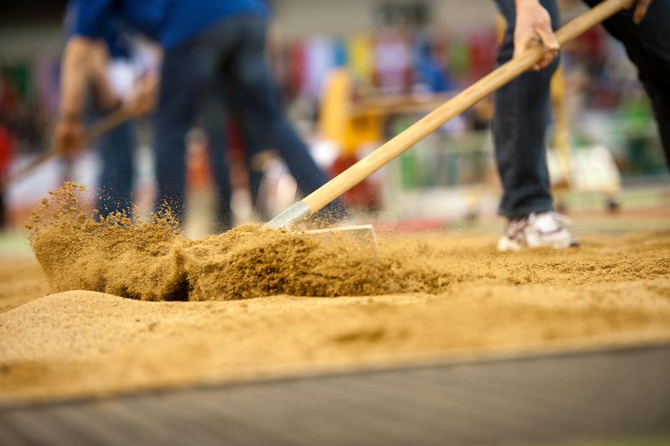 Arbeiter bearbeitet Sand mit einer Schaufel auf einem Sportplatz während einer Veranstaltung.